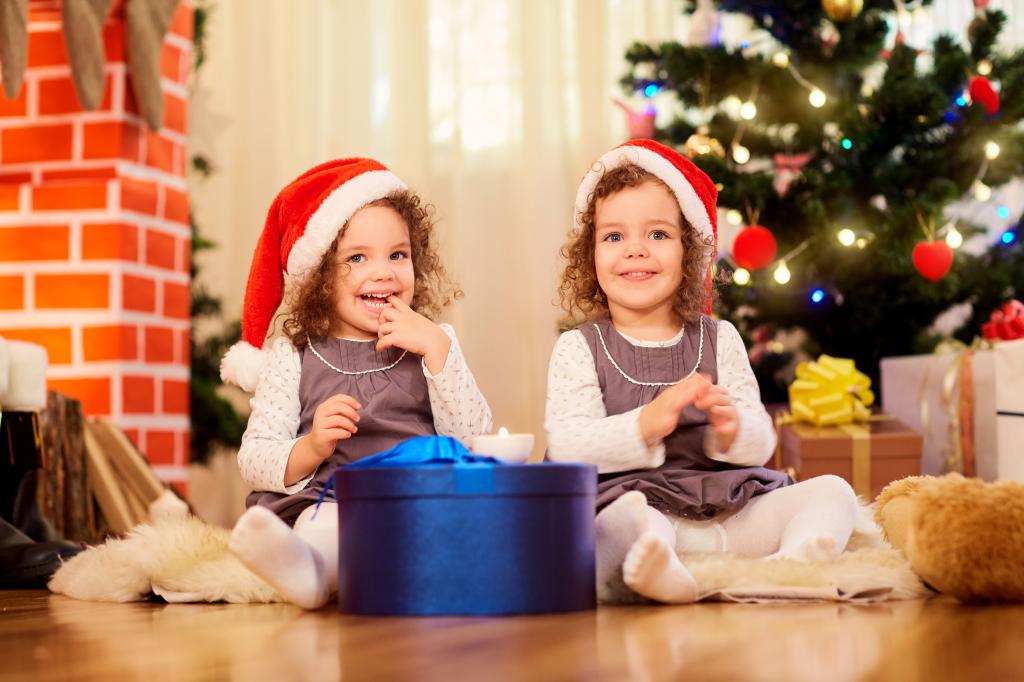 两个微笑女孩双胞胎与圣诞礼物在圣诞树下