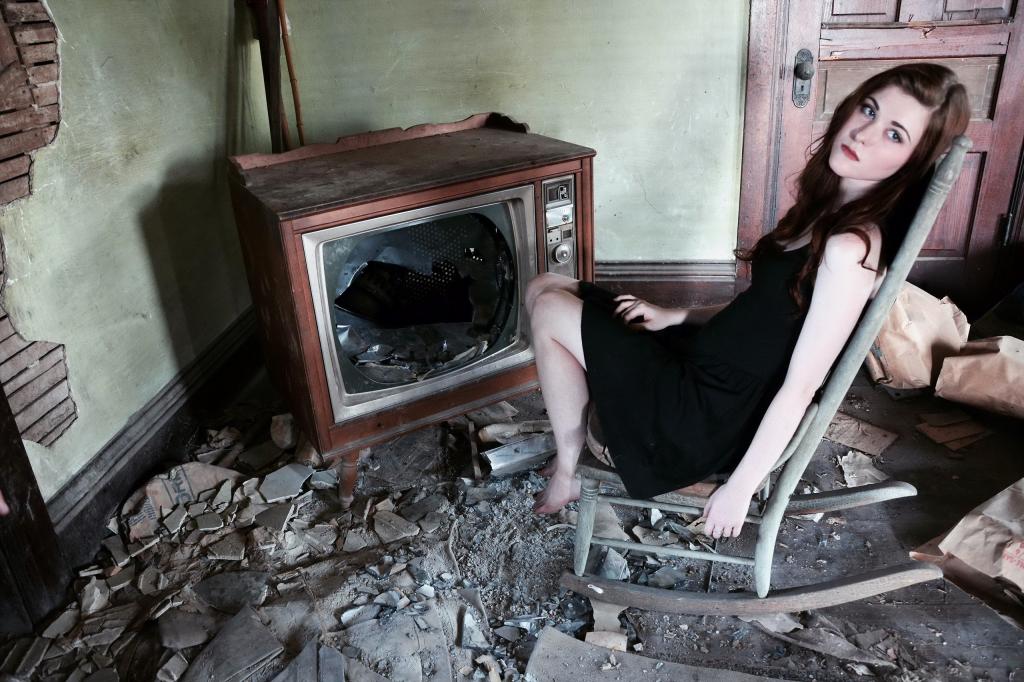 一个女孩坐在破旧的电视机旁