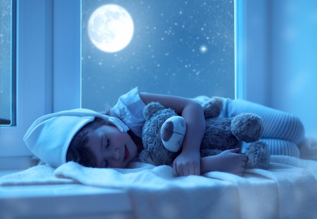 一个穿着睡衣的小孩在月亮的背景下睡着一个柔软的玩具