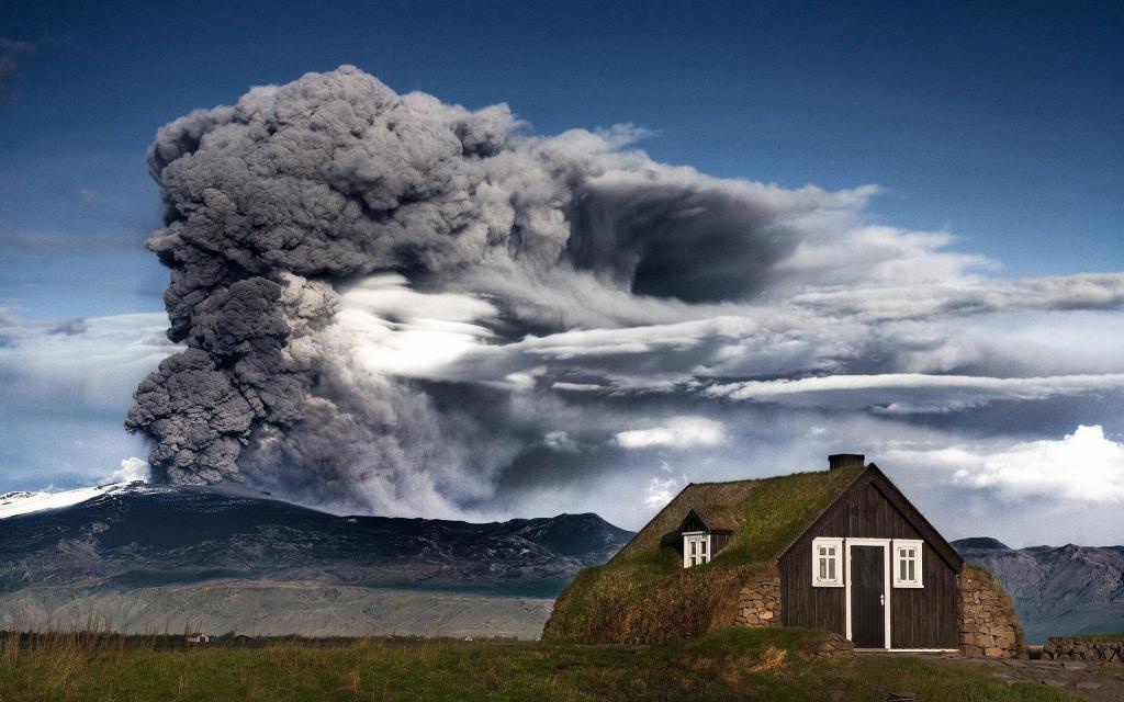 在冰岛的房子背景下的一个喷发的火山