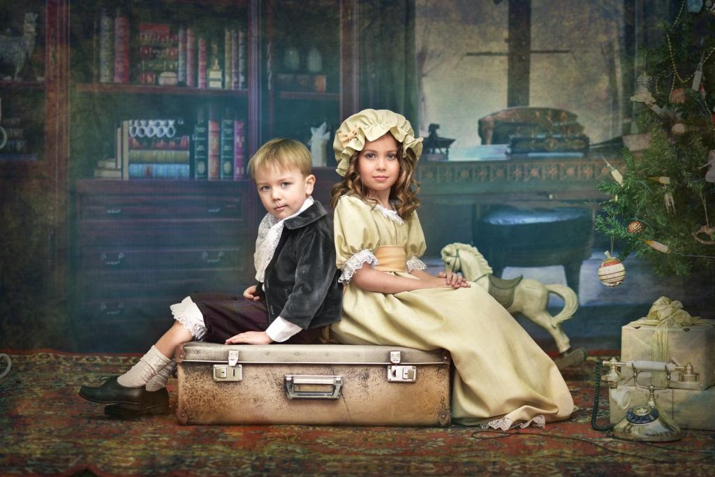 小男孩和女孩在老式的服装坐在行李箱上
