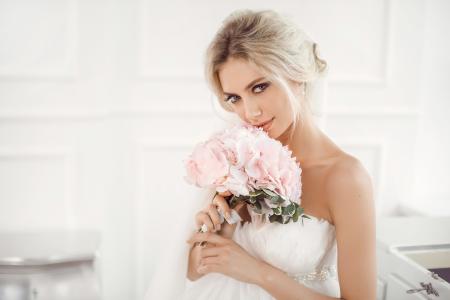 美丽的金发新娘与一束粉红色的花，在手中