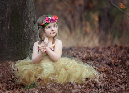 一件漂亮的衣服的小女孩坐在干燥的树叶上