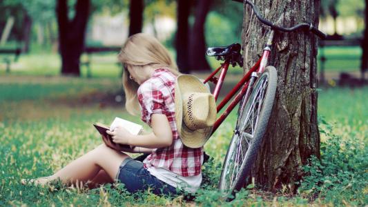 当坐在公园在草坪上时读一本书的女孩