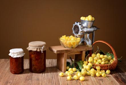 两罐果酱和黄色樱桃在一台桌子上用绞肉机