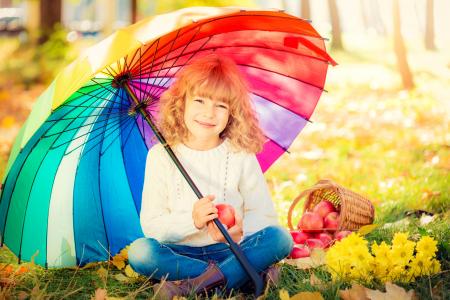 一篮苹果坐在一把五颜六色的雨伞下的小女孩微笑着