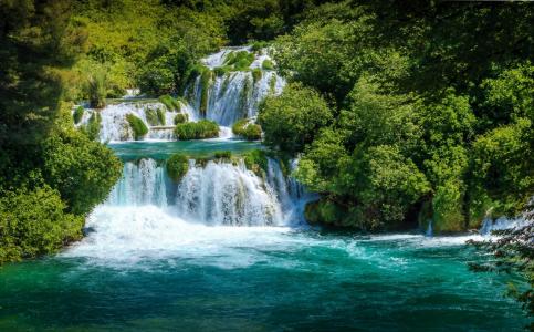 绿树旁的瀑布汹涌的蓝色的水