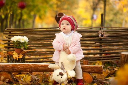 泰迪熊在秋天坐在一张木凳上的小女孩