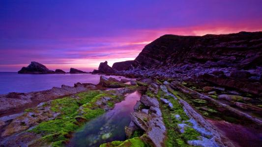 在岸边的淡紫色日落背景下的裸体悬崖