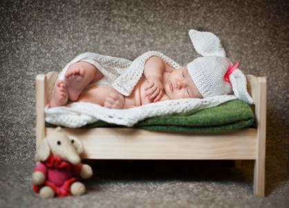 一名男婴正睡在一张白色针织兔子服装的木制床上