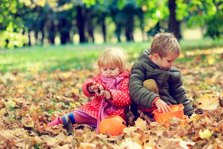 小男孩和女孩坐在黄色的树叶，在秋天的公园