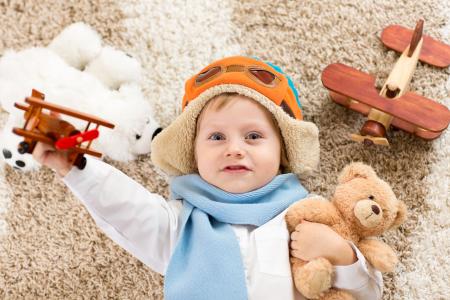 一个小男孩在一顶帽子和一架玩具飞机和一只熊在他手中