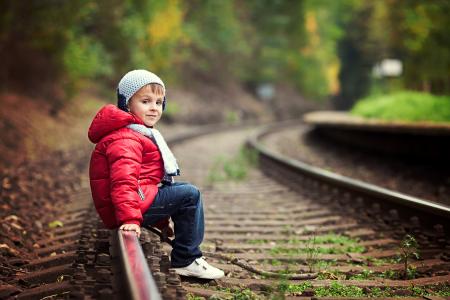 穿红色夹克的小男孩坐在铁轨上