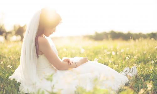 新娘的礼服的亚洲女孩坐在领域的草地上