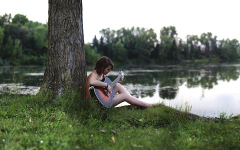 一个女孩坐在河边的一把吉他上