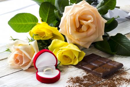一束玫瑰与巧克力和红色框与订婚戒指的桌子上
