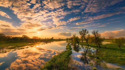 日出和云彩在河的清楚的水中被反射