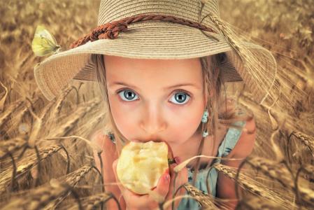 戴着帽子的小蓝眼睛的女孩吃一个苹果