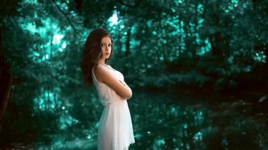 一个穿白裙子的女孩正站在一片绿色的森林里
