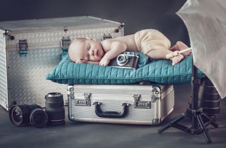 带着照相机的熟睡的婴儿睡在行李箱上