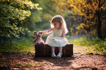 一个白色连衣裙的小女孩正坐在一个带着玩具的大手提箱里