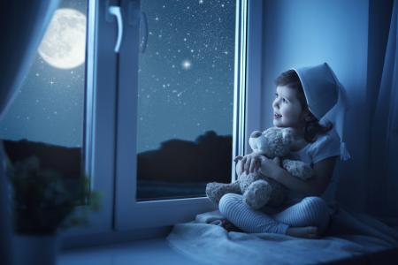 晚上，一个小女孩坐在窗台上，带着玩具