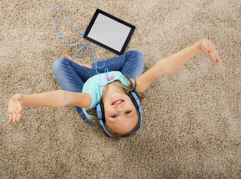 小女孩用耳机坐在地毯上听音乐