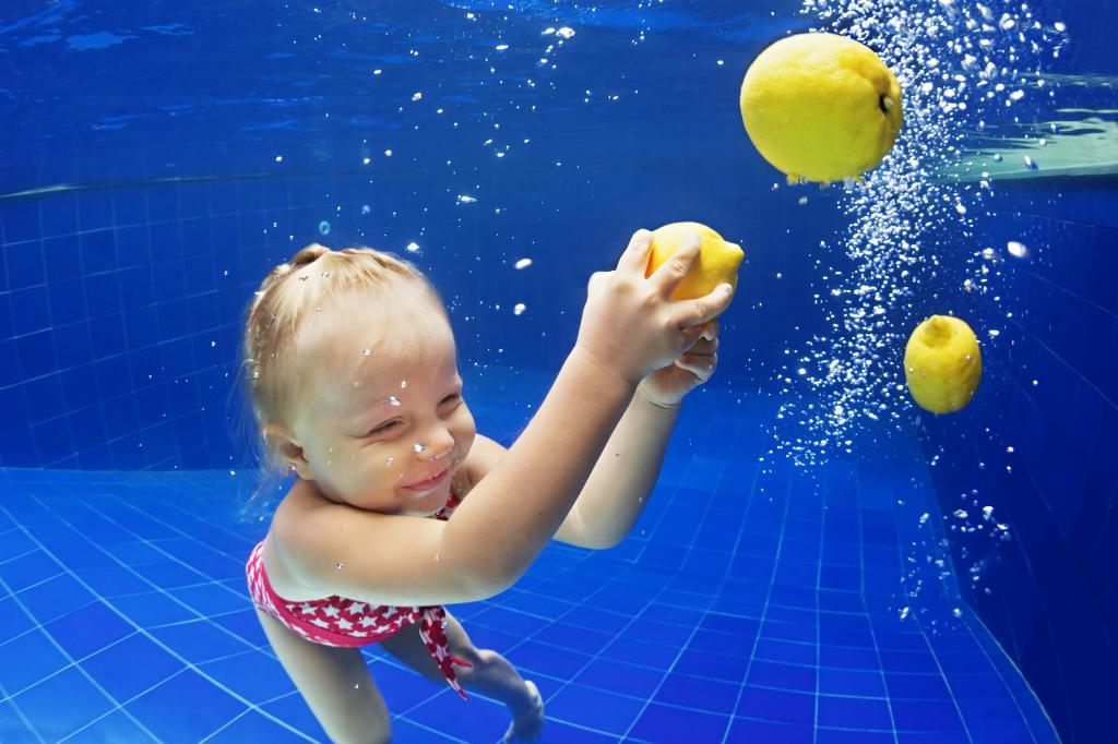 一个小女孩在游泳池里用黄色的柠檬在游泳
