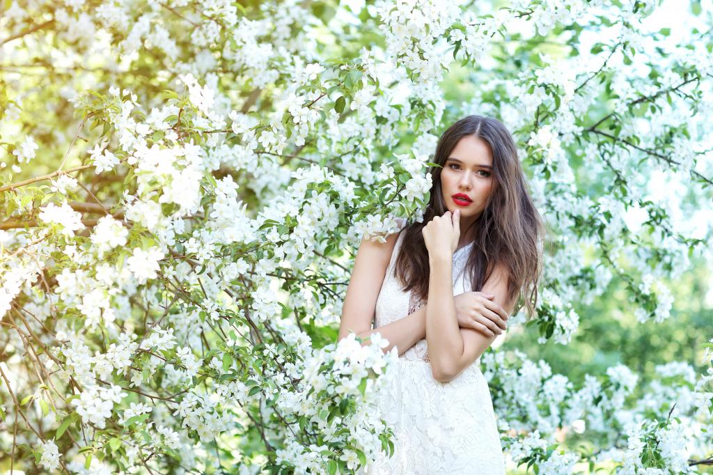 在一棵开花的树附近的白色礼服的美丽的棕发的妇女