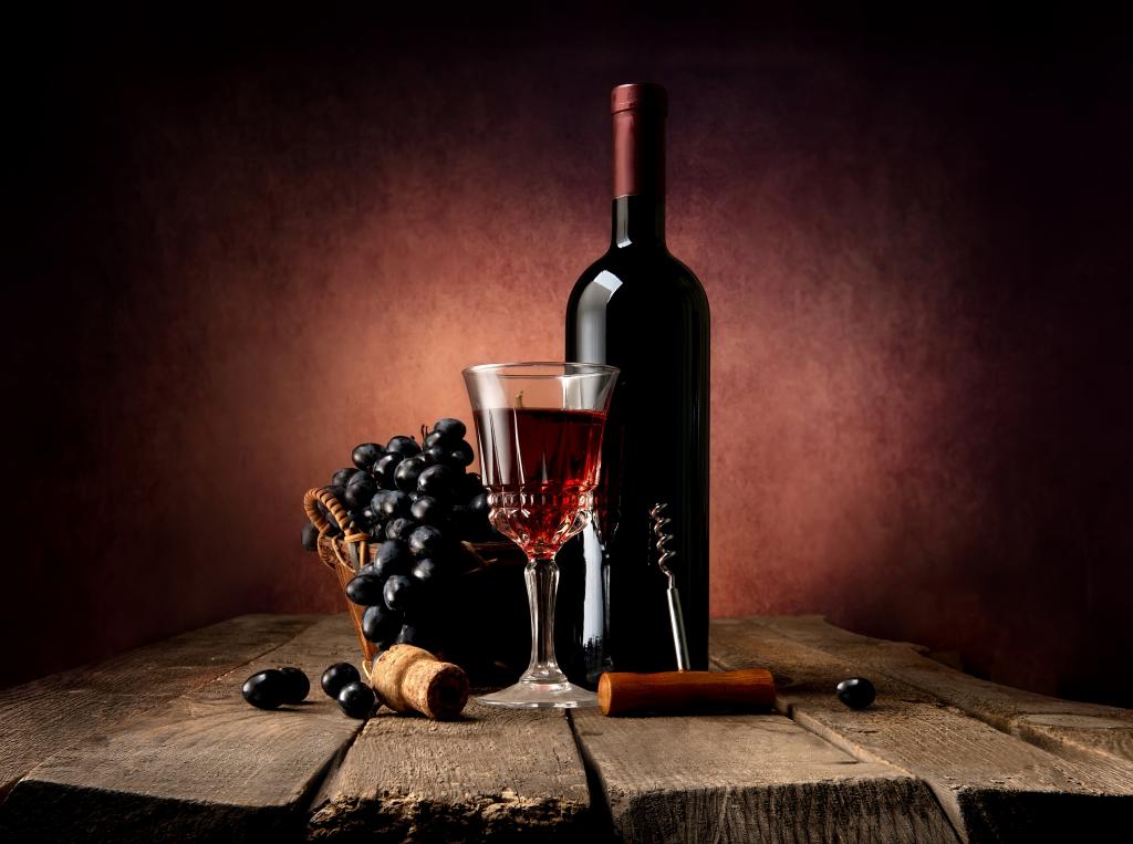 一瓶红葡萄酒放在一张桌子上，上面摆放着玻璃和蓝色的葡萄