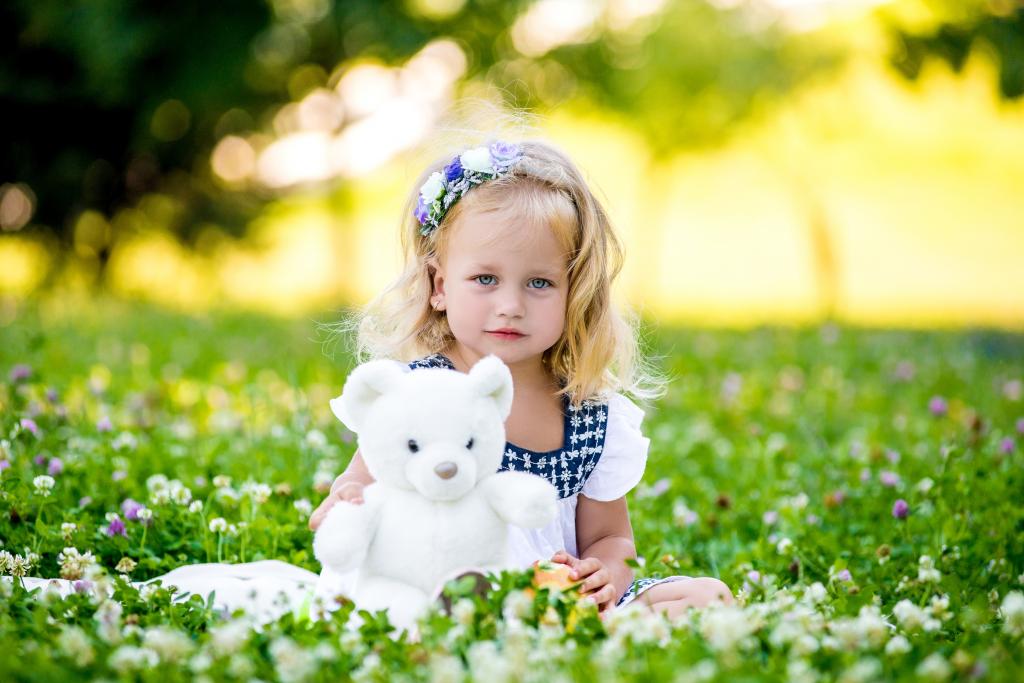 玩具的可爱小女孩坐在绿草与鲜花
