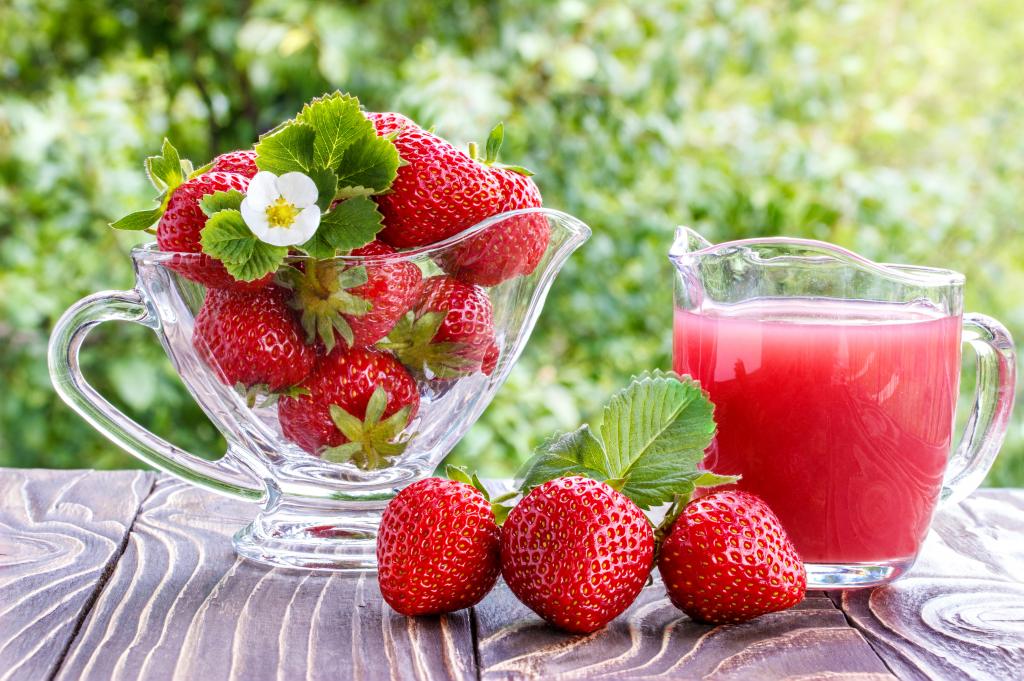 草莓汁在新鲜的草莓的桌子上的玻璃滗水器