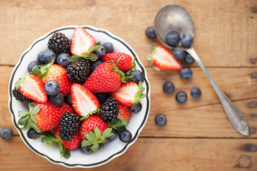 新鲜浆果的草莓，蓝莓和黑莓在木制的桌子上的盘子