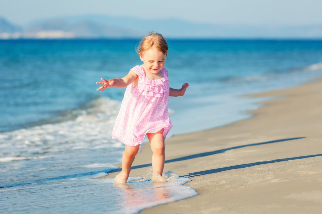 穿着粉红色连衣裙的小女孩沿着海沙漫步