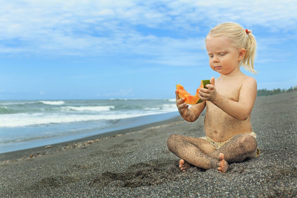 一个小女孩正坐在海边的沙地上，一片瓜子