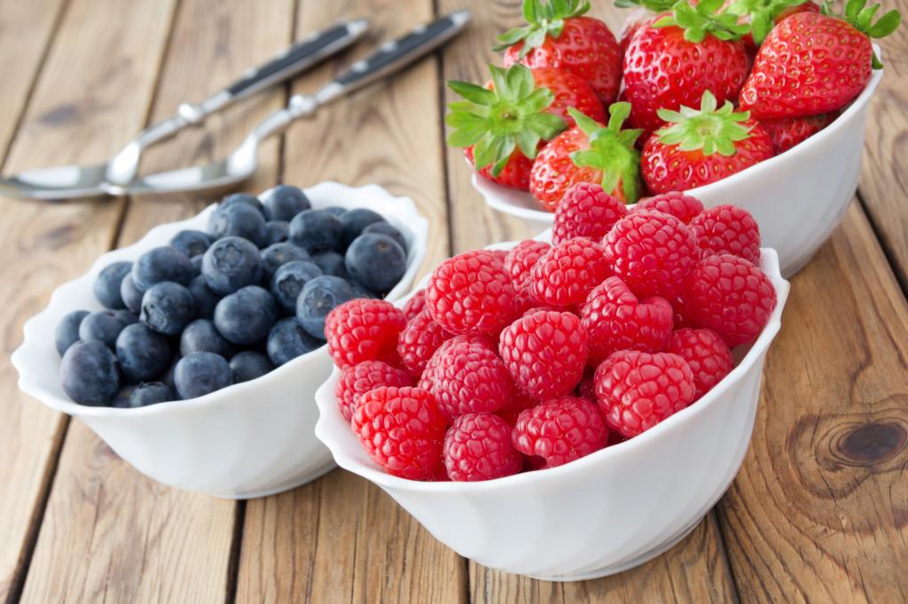 新鲜浆果的覆盆子，草莓和蓝莓在桌子上的白板