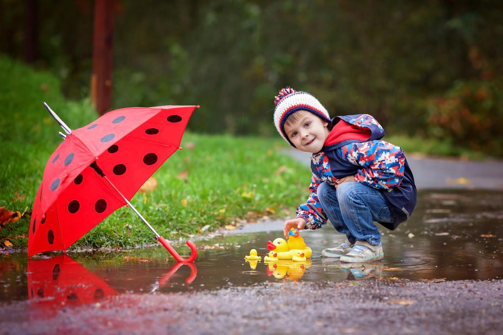 一个小男孩在雨后在一个水坑里开了一只橡皮鸭