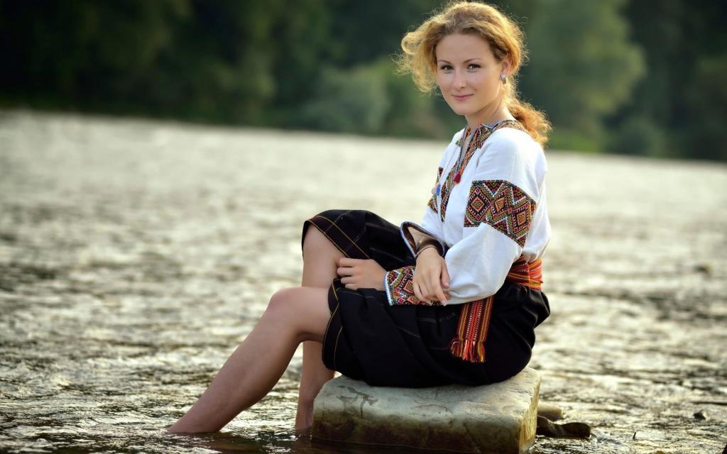 一个女孩坐在传统服装的水边的石头上