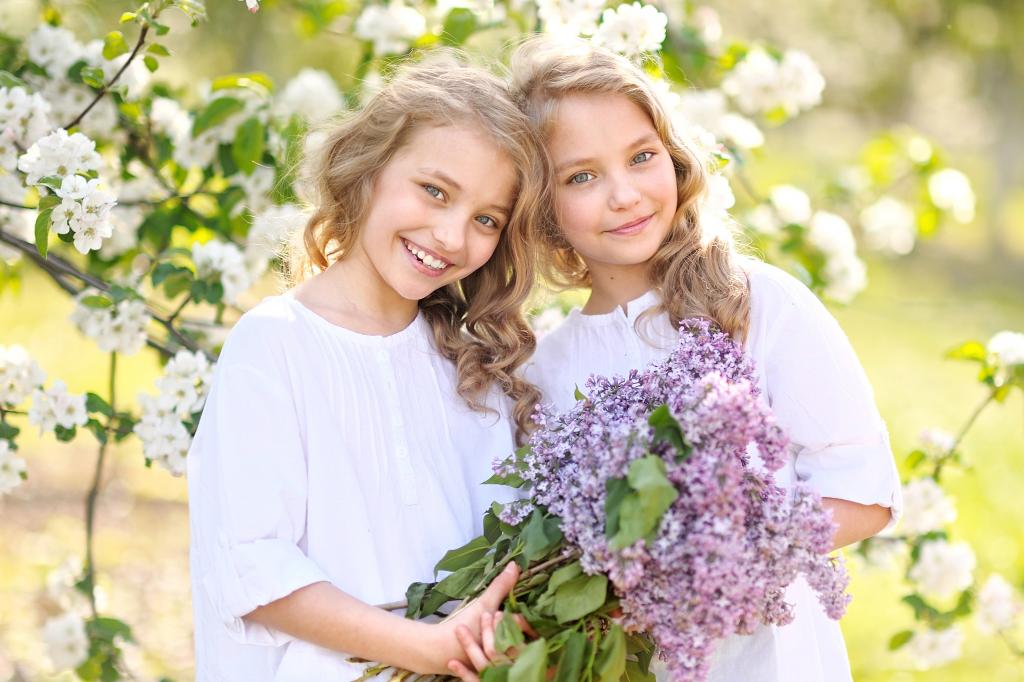 两个微笑的女孩双胞胎与丁香花束
