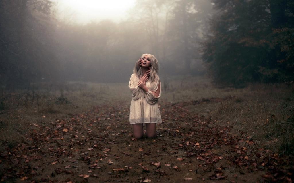 白色礼服的金发女郎跪在森林中