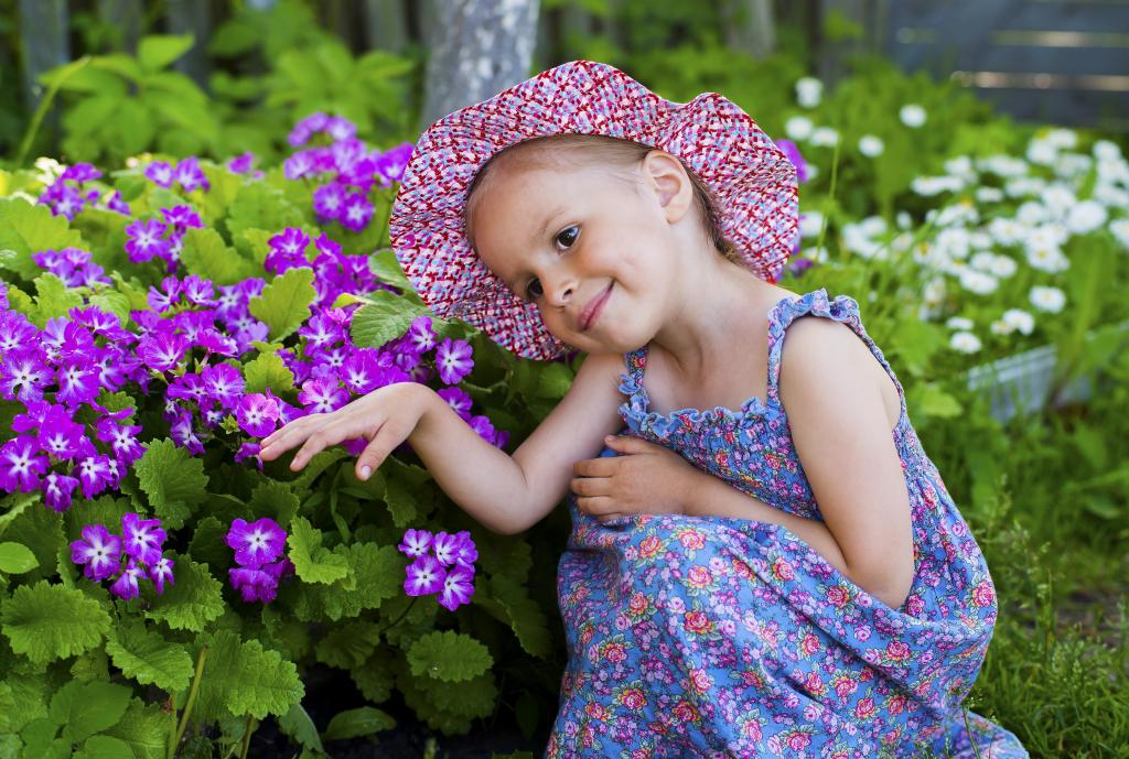 在紫色的花旁边的一顶帽子的小女孩