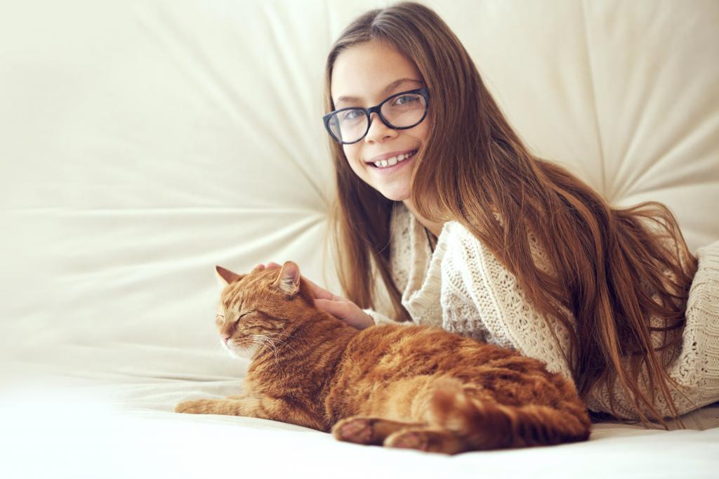 戴着眼镜抚摸一只红色的猫的棕发女人的微笑女孩