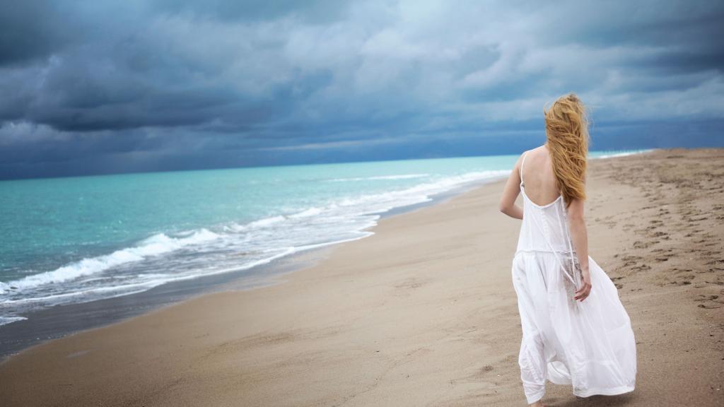 穿白裙的女孩正沿着海滩散步