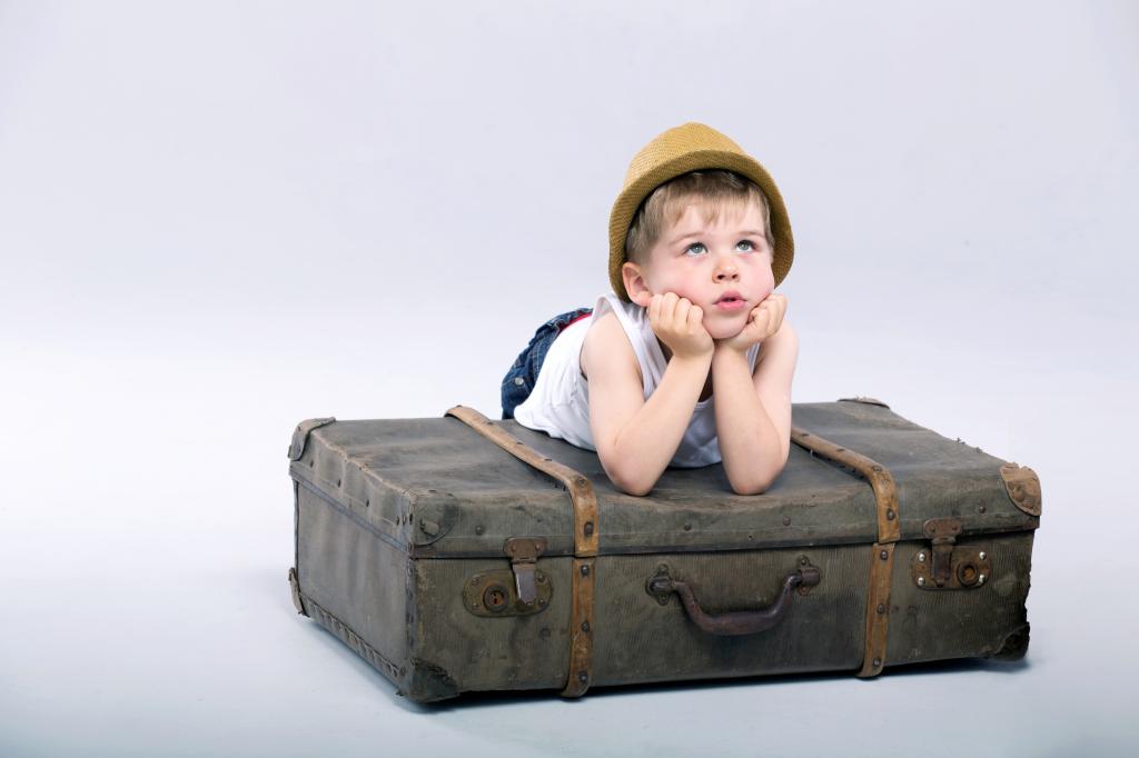 一个小男孩躺在一个灰色的背景上的大手提箱