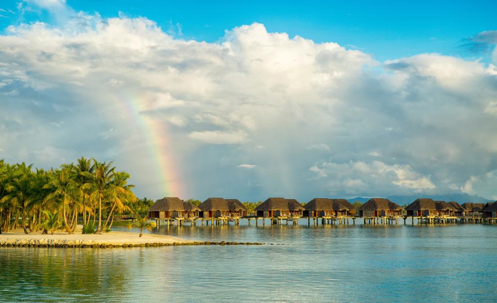 平房在热带海滩上与彩虹多云的天空下的水中