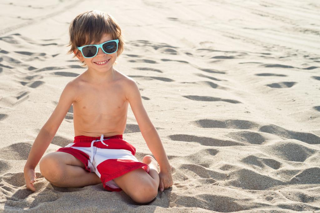 戴眼镜的小男孩坐在沙滩上的沙子上