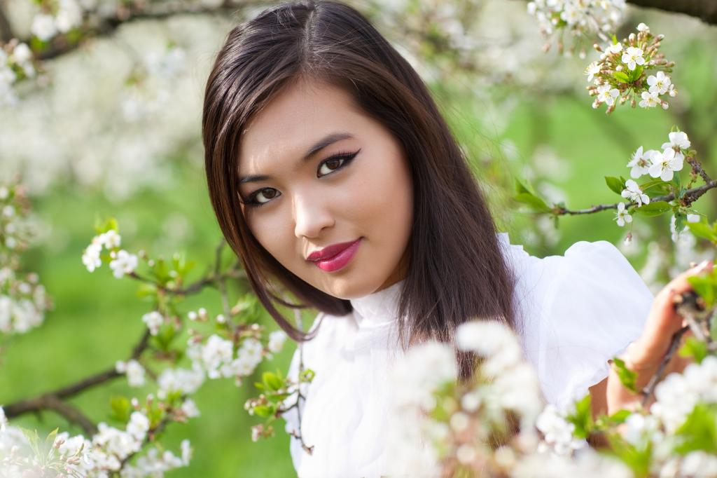 美丽的亚裔女孩在一棵开花的树的分支