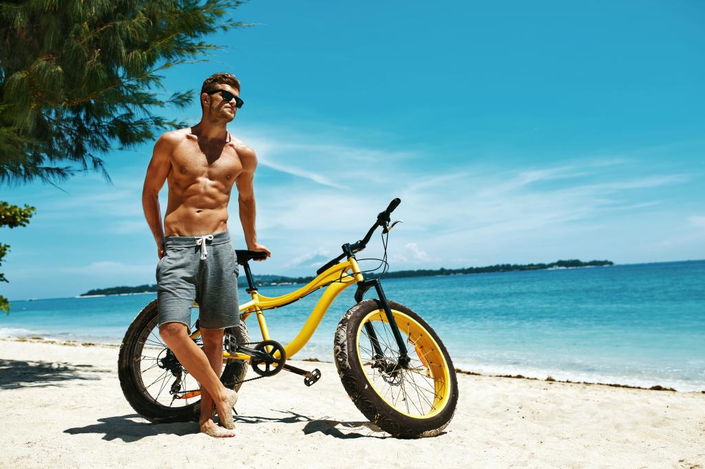 英俊的肌肉男与一辆自行车在海滩上
