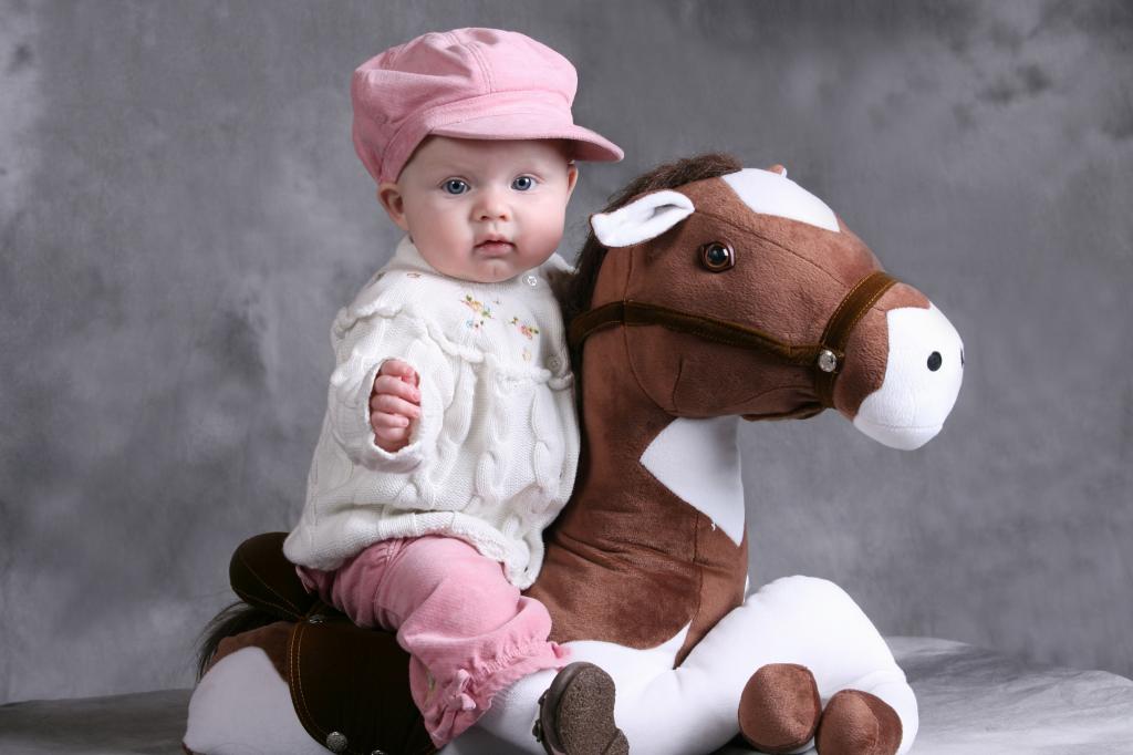 粉红色的帽子的小女孩坐在玩具马